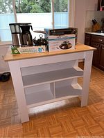 Front view of white kitchen island with natural wood top and multiple shelves, kitchen appliances placed on top.