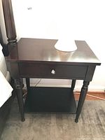 Front and top view showing one drawer with metal knob and lower shelf. Surface has scratches though still glossy.