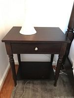 Dark brown Martha Stewart nightstand showing front and top surface with lamp.
