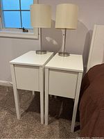 Nightstands placed side by side with lamps on top, showing white MDF finish and simple square design.