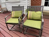 Two gray metal outdoor chairs with green cushions placed on a red wooden deck.