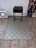 Photo showing the entire side table on top of the indoor/outdoor rug with diamond pattern, both placed on carpeted floor.