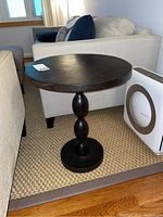 Full view of a dark stained wooden round side table with a turned pedestal base, showing overall design and scale next to furniture.