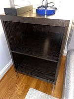 Front view of the dark wood side table showing two open shelves and wood grain surface