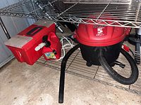Photo of red 5 gallon Shop-Vac Quiet Series 2.0 peak HP with attached hose under metal shelving.