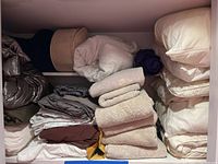 Closet shelf with neatly folded towels, pillows, sheets, and a fabric storage bin