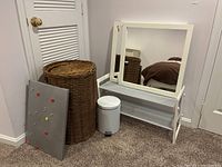 Three square white framed wall mirrors, white shoe rack, wicker hamper, metal mesh bulletin board with magnets, and small white pedal waste basket arranged in a corner.