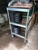 Front view of the metal wire rolling rack with three tiers, showing rust on shelves and caster wheels at the bottom.