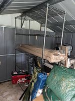 Full view of shelving unit with some items placed on shelves. Unit appears to be constructed of black metal wire with visible rust spotting and wear.