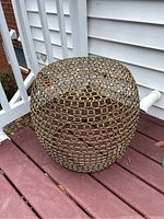 Full view of the round wire mesh side table situated on outdoor deck flooring beside a staircase and siding of a building.