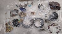 Multiple costume jewelry pieces lying on a white fluffy surface inside clear plastic bags showing bracelets, rings, necklaces, brooches.