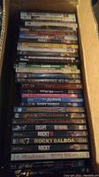 Photo of a box filled with DVDs and Blu-ray movies stacked vertically showing spines with titles.
