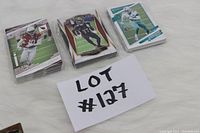 Three stacks of football cards in clear plastic, laid on white surface with lot number card.
