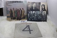 Three Foreigner vinyl LP records laid out showing cover artwork, including a group photo album cover, a black and white photos cover, and a grey '4' album cover.