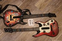 Two Guitar Hero guitar controllers placed side by side on the floor, showing top and neck details with lots of colorful stickers