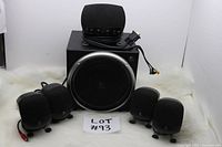 Photo of all items in the set showing four satellite speakers, subwoofer, and control pod with cables.