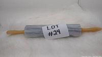 Marble rolling pin featuring wooden handles at both ends, placed on a white surface with a label reading 'LOT #24'.