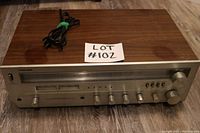 Front angled view showing the wood grain top, silver front panel with multiple control knobs, power cord on top, and lot number card.