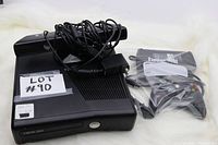 Xbox 360 S model console with power supply cable shown on top and a separate wireless controller packaged in plastic.