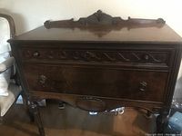 Photo showing front view of mahogany buffet cabinet with carved front panels and ornamental crest on top back edge.
