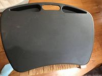 Front view of the black laptop holder showing its rectangular shape with rounded sides and two handle holes at the top.