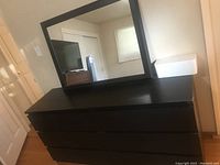 Overall view of dark brown IKEA dresser with six drawers and large rectangular mirror on top.