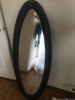 Full view of the oval mirror with leather frame showing peeling and scratches on the leather.