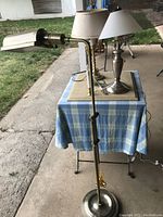 Full view of the adjustable height floor lamp along with three table lamps on a blue checkered tablecloth outdoors.
