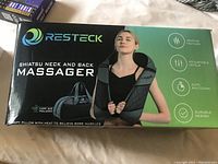 Front of the RESTECK Shiatsu Neck and Back Massager box showing product image and key features: heating feature, adjustable levels, auto shutdown, durable design.