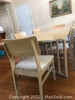Dining table with natural light brown rectangular surface and adjustable legs, surrounded by six matching chairs