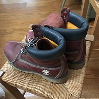 Back and side view of Timberland brown vintage leather boots on woven chair. Shows padded collars, embossed Timberland tree logo on heel, and overall condition with creases.