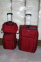 Front view of three red luggage pieces showing large upright suitcase, medium carry-on luggage, and small shoulder bag with telescoping handles.