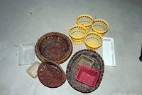 Photo showing an assortment of 12 baskets on a floor including yellow plastic baskets, white plastic baskets, and several brown woven willow baskets of varying shapes and sizes.