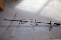 Full view of the stainless steel rotisserie spit rod showing black handle on one end and pronged forks.