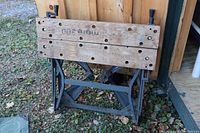 Folded workbench showing wooden top boards with multiple holes and metal frame at ground level outdoors