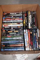 Box filled with stacked DVD movie cases showing various action, adventure, and sci-fi titles