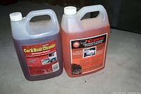 Two plastic gallon containers of pressure washer detergents. One labeled Car & Boat Cleaner, the other Kodiak Car & Boat Wash & Wax. Both containers partially filled with liquid and placed inside a cardboard box.