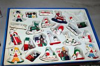 Wooden Christmas decorations set in plastic tray, various small painted figurines and shapes including Santa, snowmen, nutcracker, reindeer, toy train, rocking horse, Christmas blocks spelling NOEL