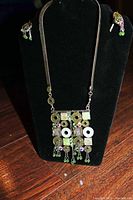Full view of the necklace displayed on a black stand alongside matching earrings.