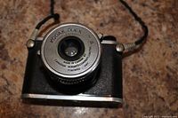 Front view of Kodak Duex camera showing lens and textured body with neck strap on granite surface