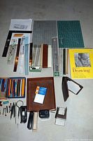 Overview of lot showing rulers, staplers, drawing pad, cutting mats, colored pencils, pens, and wooden file basket