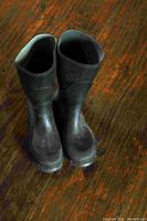 Front view of the pair of black rubber boots on wood floor showing shape and sole.