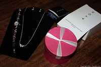 Photo showing Avon branded box, red gift box, watch, necklace, and earrings displayed on black jewelry holder.