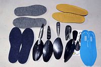 Photo showing 4 pairs of insoles in different colors and textures, 2 pairs of black shoe stretchers, and 2 black shoe horns on a plain surface.