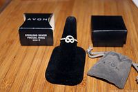 Photo of the Avon sterling silver pretzel ring on a black ring display with its box and pouch in the background.