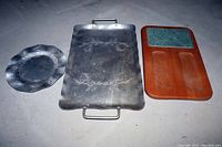 Shows 3 aluminum trays: a round tray with scalloped edges, a large rectangular tray with floral engraving and handles, and a wooden cheese board with a marble cutting insert and compartments