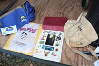 Photo of camping items including blue Plasson camp sink, Wet Wear protective clothing in package, two books, and canvas shoulder bag