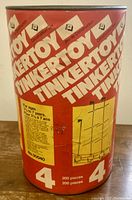 Red cylindrical metal container with white Tinkertoy logos and number 4, with age recommendation and piece count labels