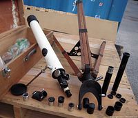 Telescope and accessories laid out on wood crate with lens caps, eyepieces, and other parts visible