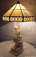 Front angled view of the carved alabaster figural lady lamp with stained glass shade illuminated.